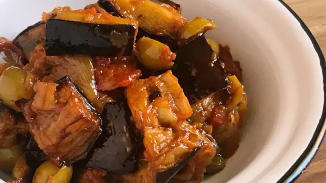 Un plato de caponata siciliana, con berenjenas, aceitunas y tomate, servido en un cuenco blanco.