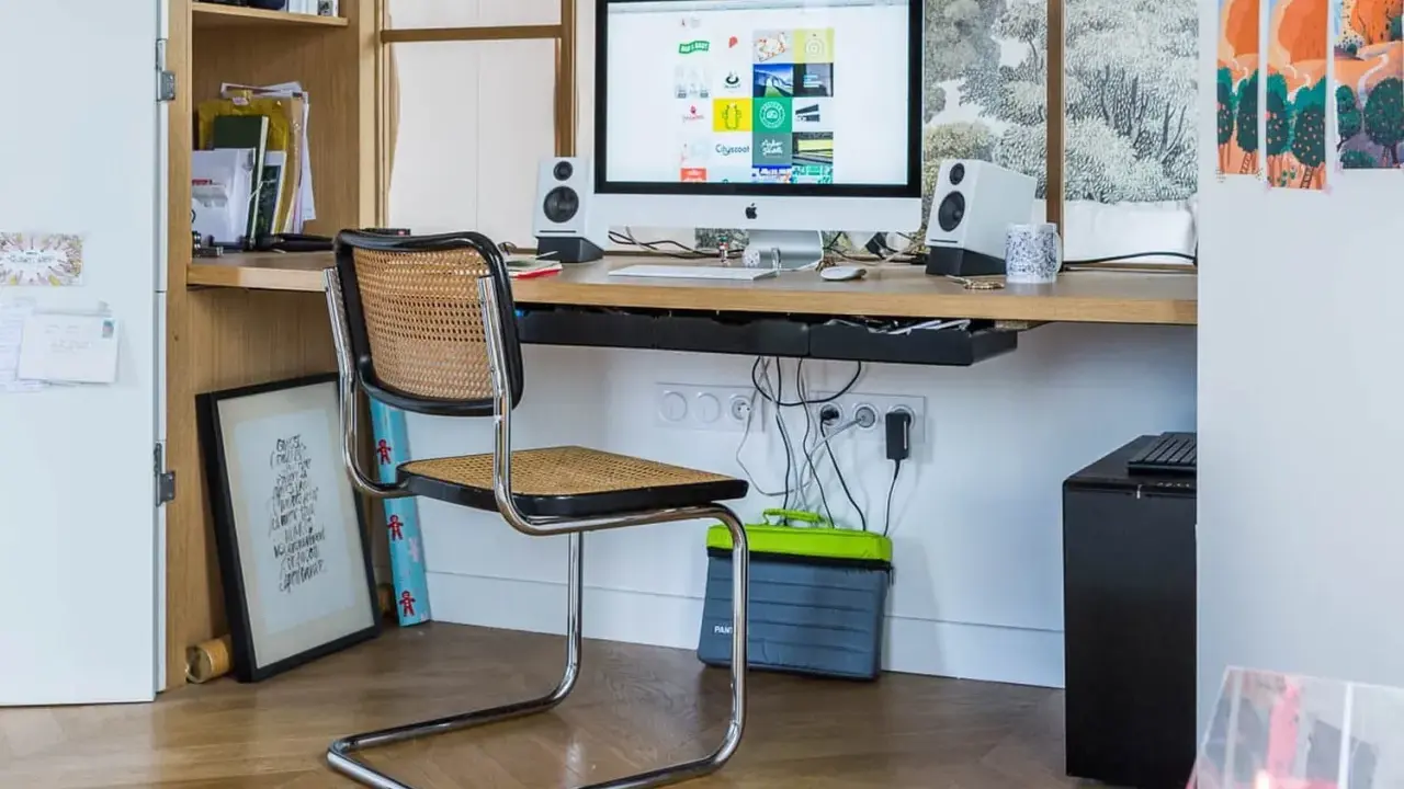 Bureau moderne avec iMac, chaise en rotin et étagères. Idéal pour savoir comment choisir un ordinateur de bureau adapté à votre espace de travail.