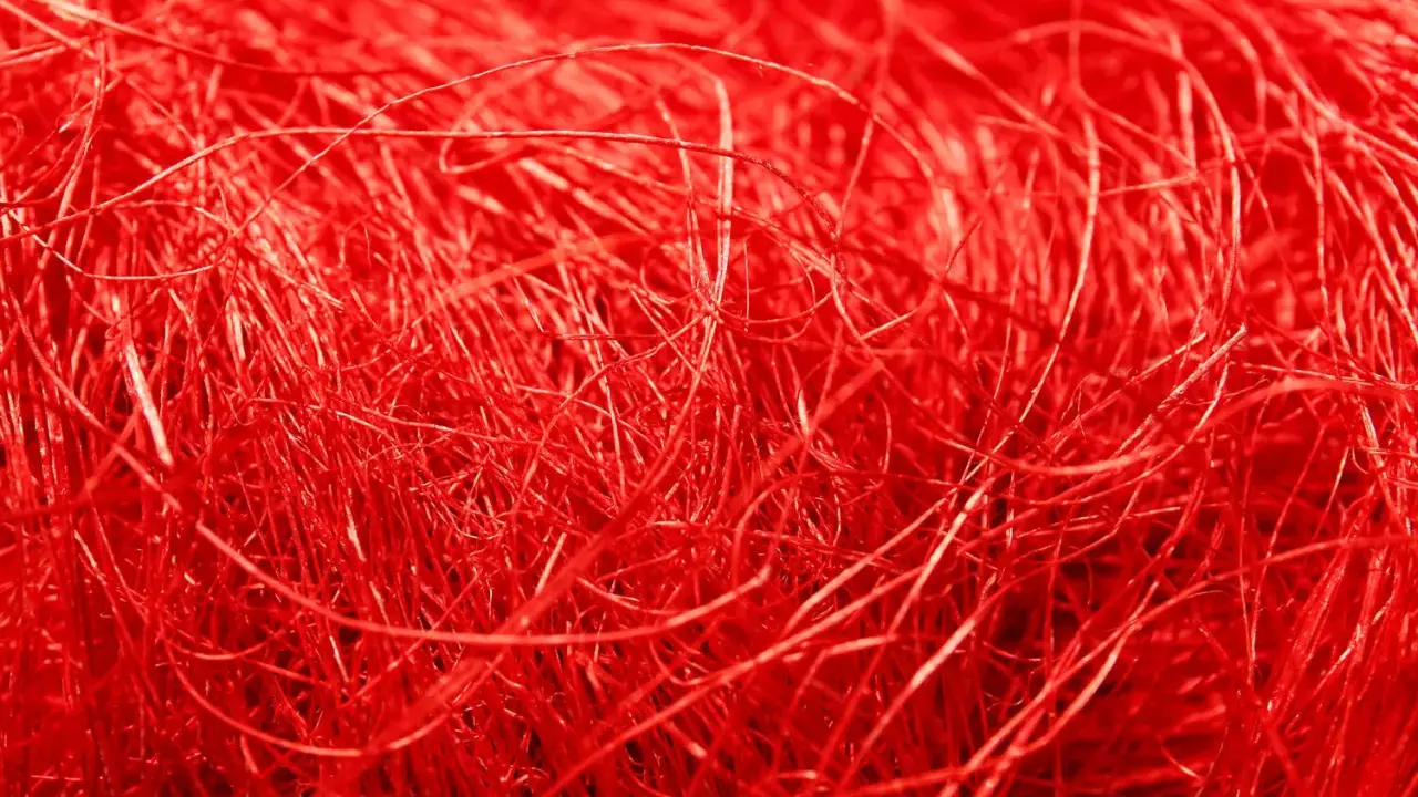 Un groviglio di fili rossi vibranti, una **fibra artificiale** che ricorda un nido intricato o capelli mossi dal vento.