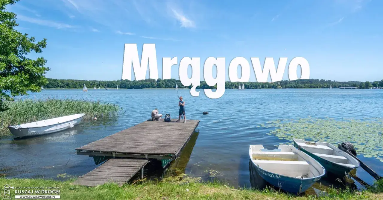 Mrągowo atrakcje: spokojny dzień nad jeziorem, dzieci łowią ryby z pomostu, żaglówki na horyzoncie.