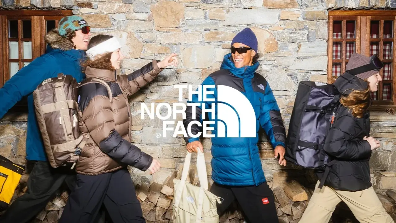 Cztery osoby w kurtkach The North Face, z plecakami i torbami, na tle kamiennej ściany. Jak rozpoznać podróbkę? Sprawdź detale!