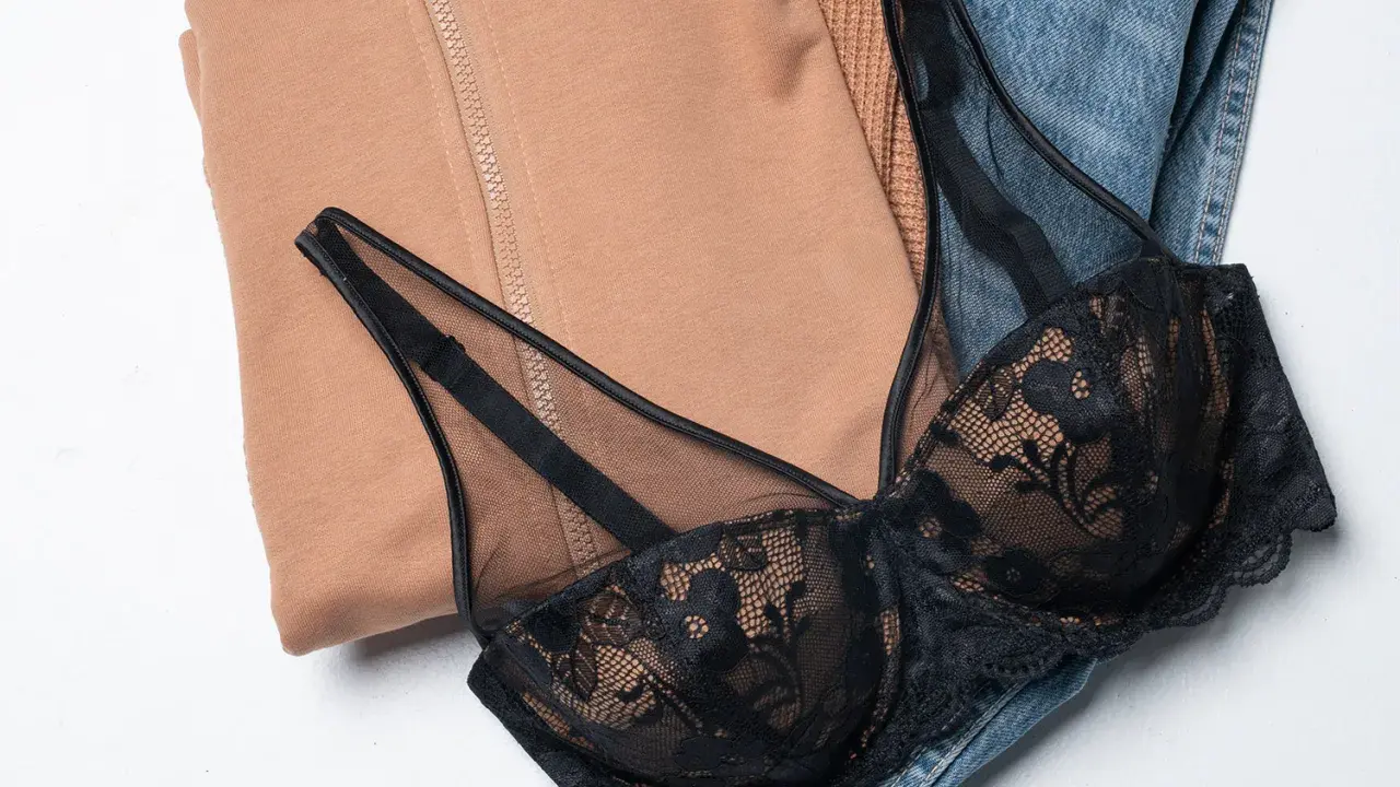 Un reggiseno di pizzo nero adagiato su jeans e felpa color cammello. Pensando a ogni quanto si cambia il reggiseno, questo è un capo che merita cura.