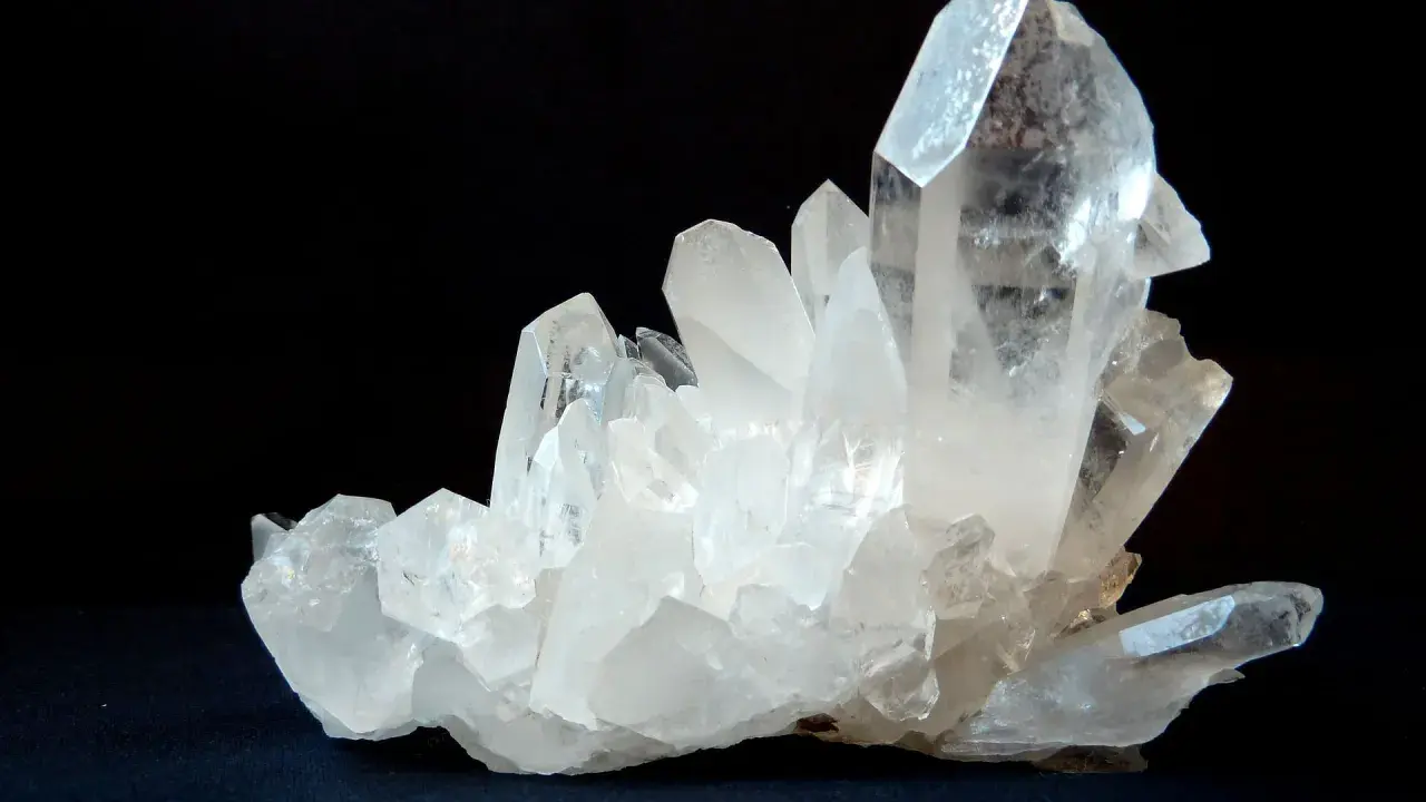 Un grappolo di cristalli di quarzo trasparenti e luminosi su sfondo scuro. Questo è un esempio di che cos'è il quarzo, un minerale comune e versatile.