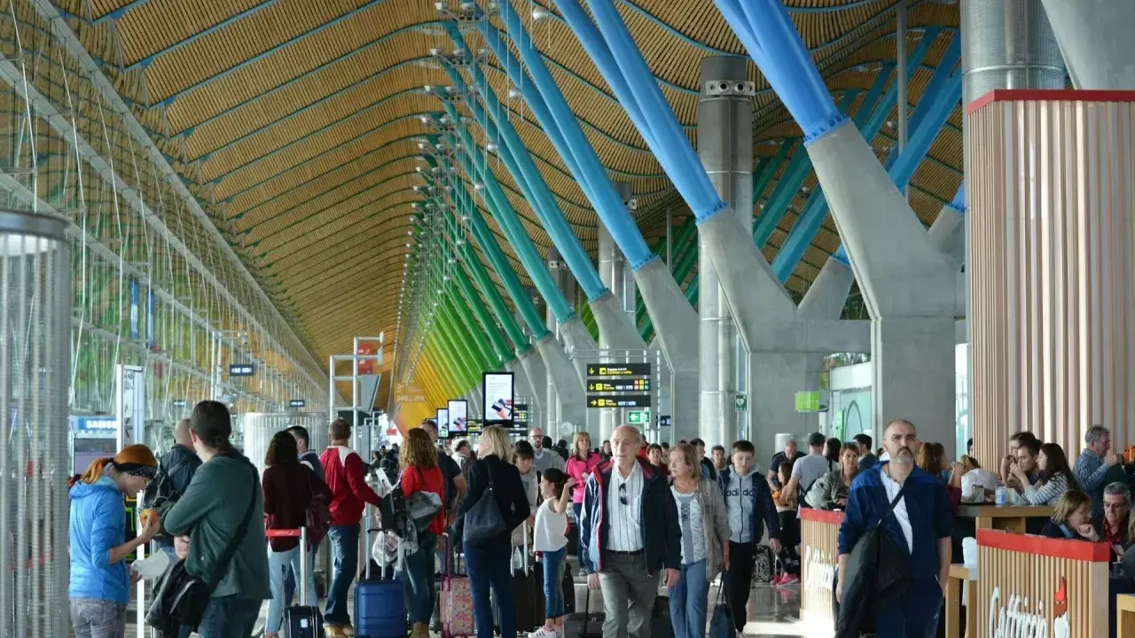 Ludzie z bagażami w nowoczesnym terminalu, jednym z wielu lotnisk w Europie, podziwiają architekturę z kolorowymi podporami.