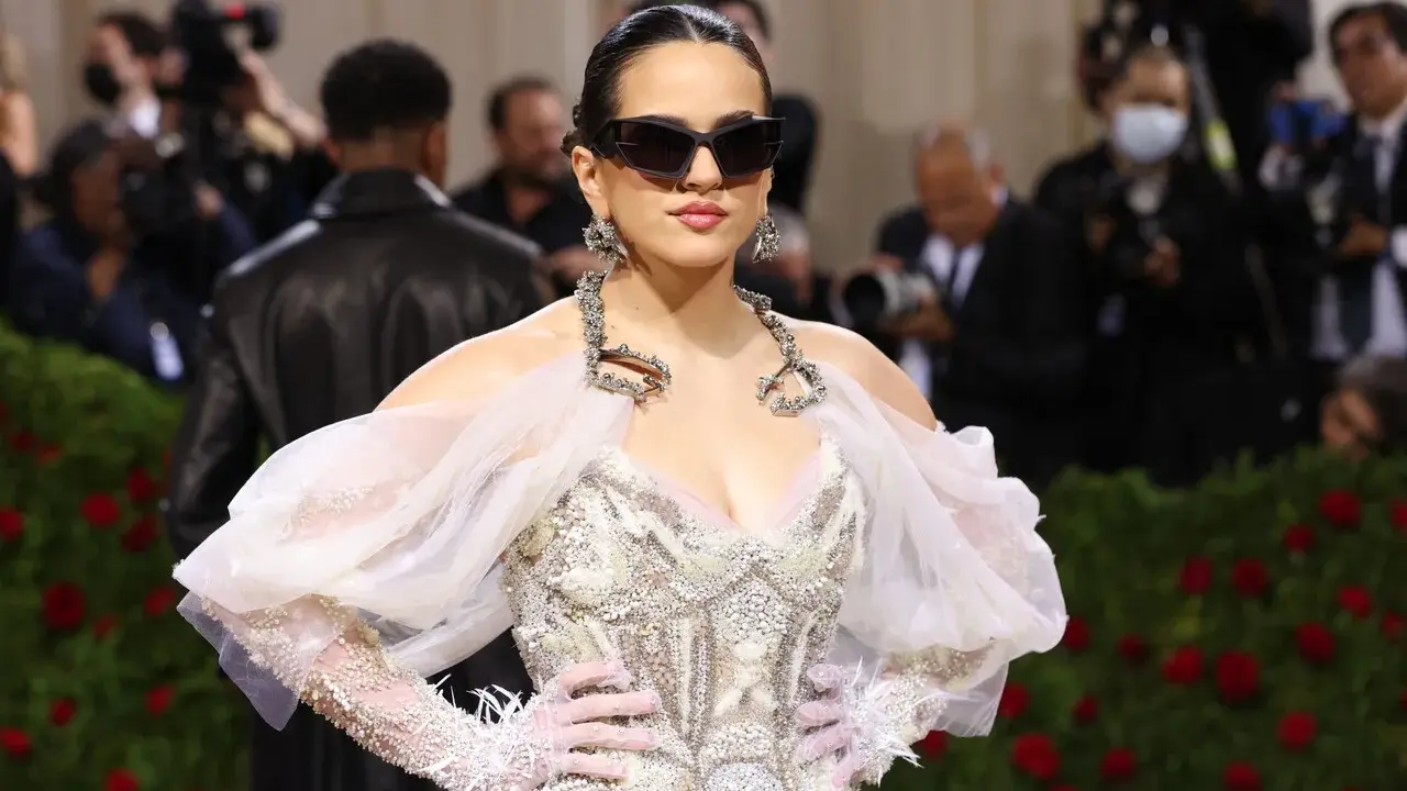 Rosalía deslumbrante en la Met Gala, con un vestido blanco adornado y gafas de sol vanguardistas.