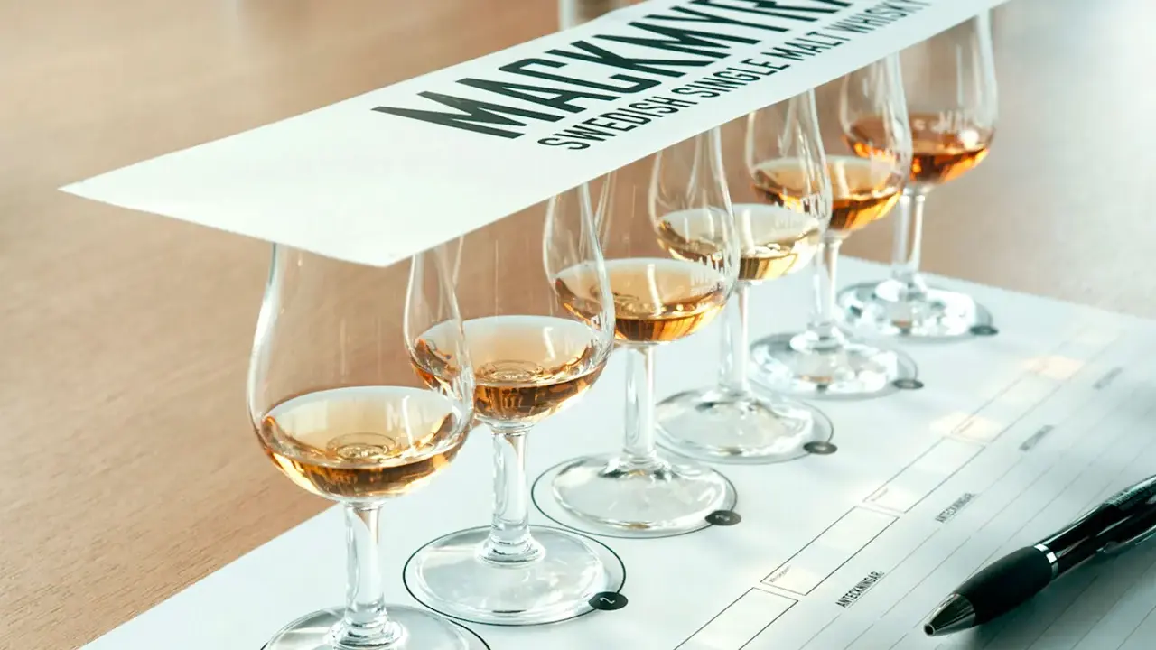 Mackmyra whiskyprovning med sex glas gyllene whisky uppradade på ett bord. En penna ligger redo för anteckningar.