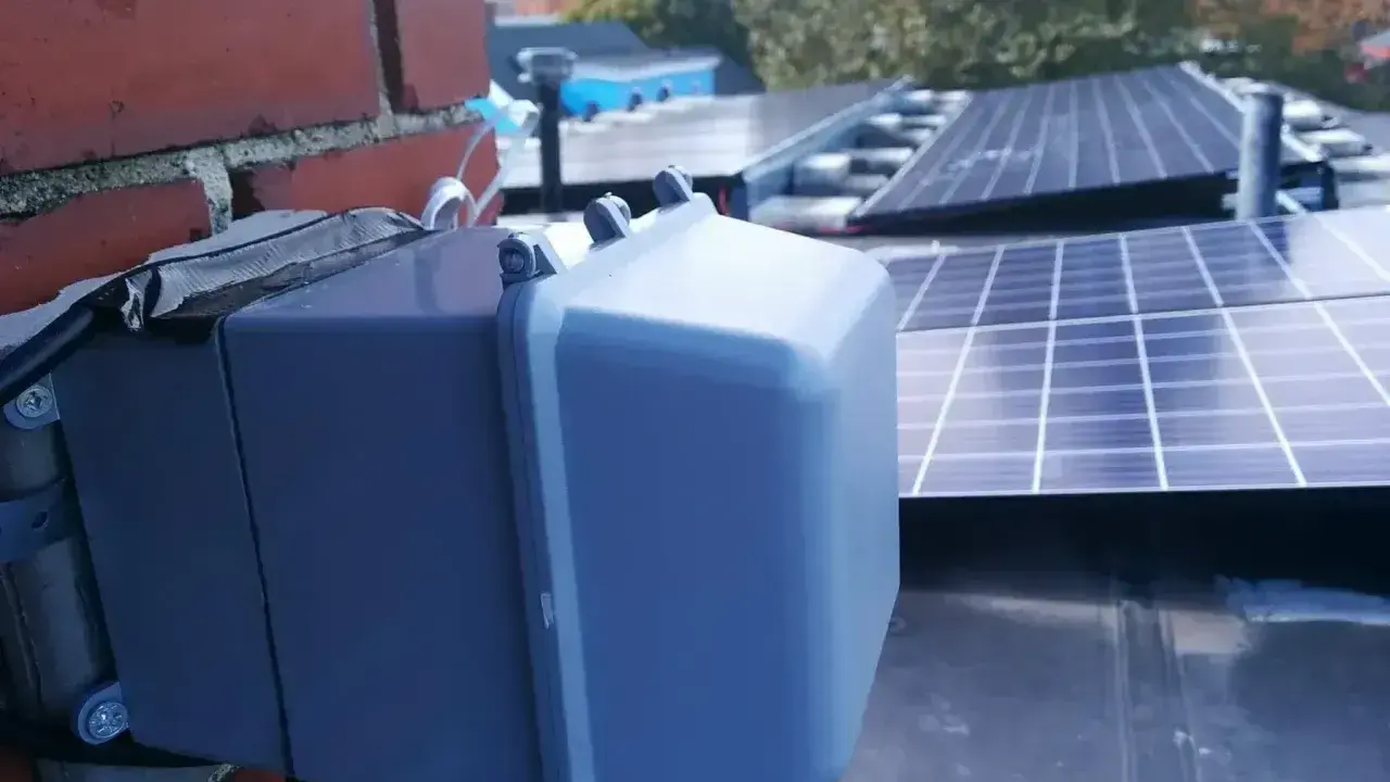 System podgrzewania paneli fotowoltaicznych zamontowany na dachu, obok ceglanej ściany.