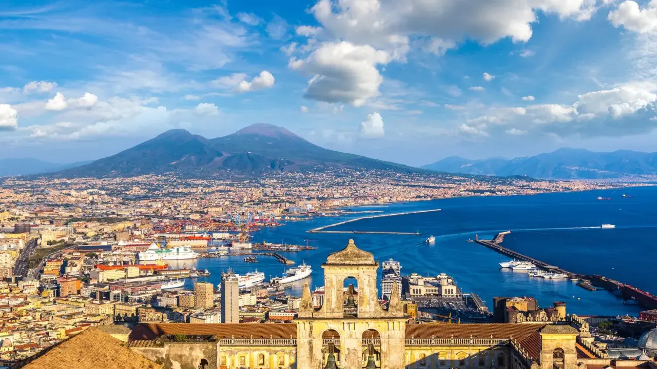 Vista di Napoli con il Vesuvio sullo sfondo, un porto vivace e un campanile antico. Un gioiello tra i siti UNESCO Campania.