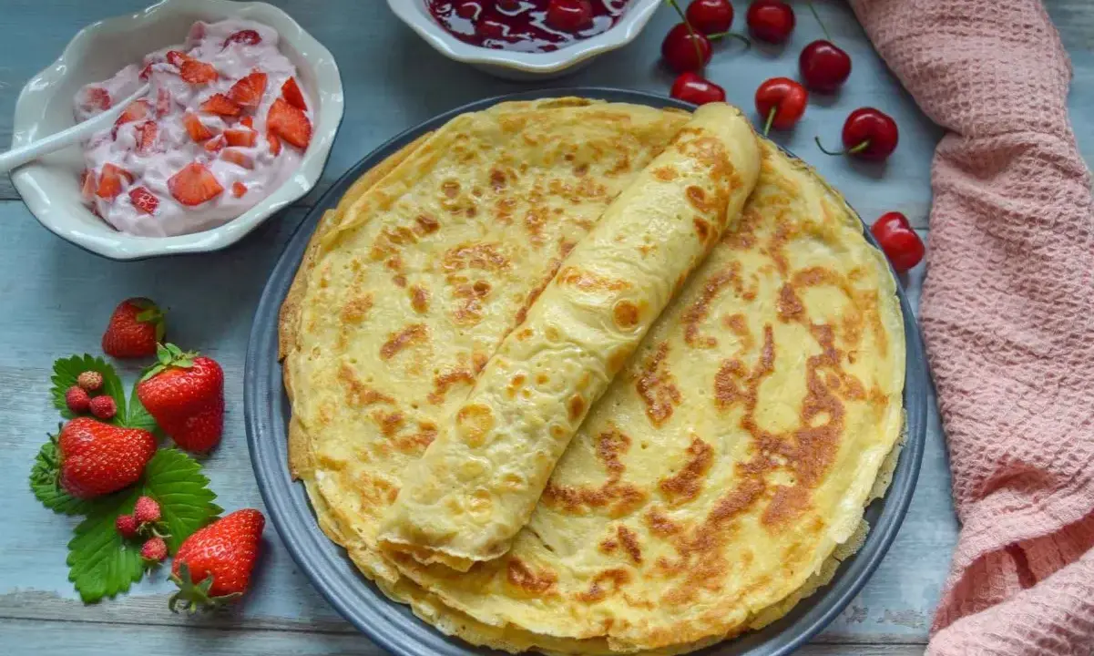 Omas Pfannkuchen-Rezept: goldbraune Pfannkuchen auf einem Teller, dazu Erdbeerquark, Kirschmarmelade und frische Erdbeeren.