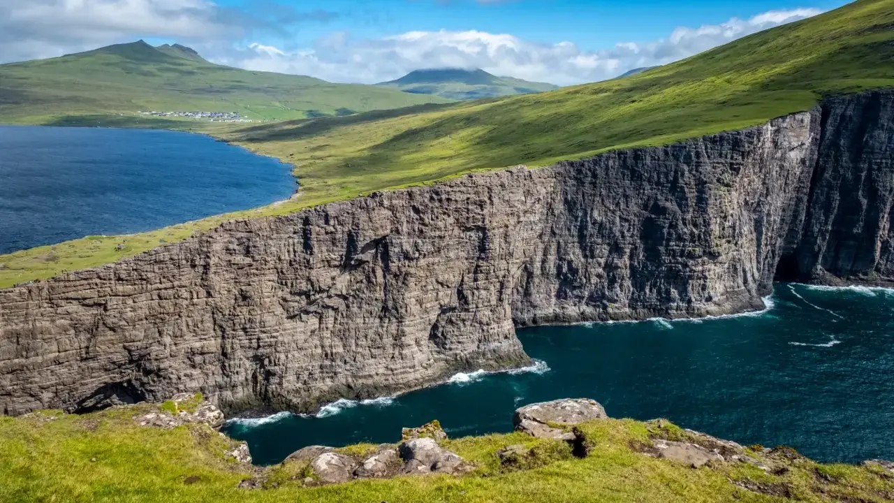 Scogliere imponenti e un lago blu intenso nelle Isole Faroe, dove gli abitanti vivono in armonia con la natura selvaggia.