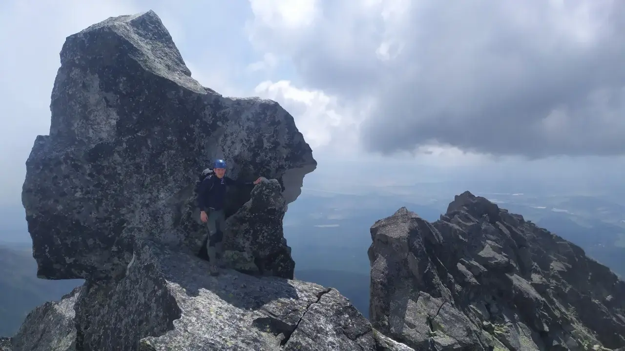 Wspinacz w kasku na skalistym szczycie, podziwiający widok. Tatry poza szlakiem, gdzie każdy krok to przygoda.