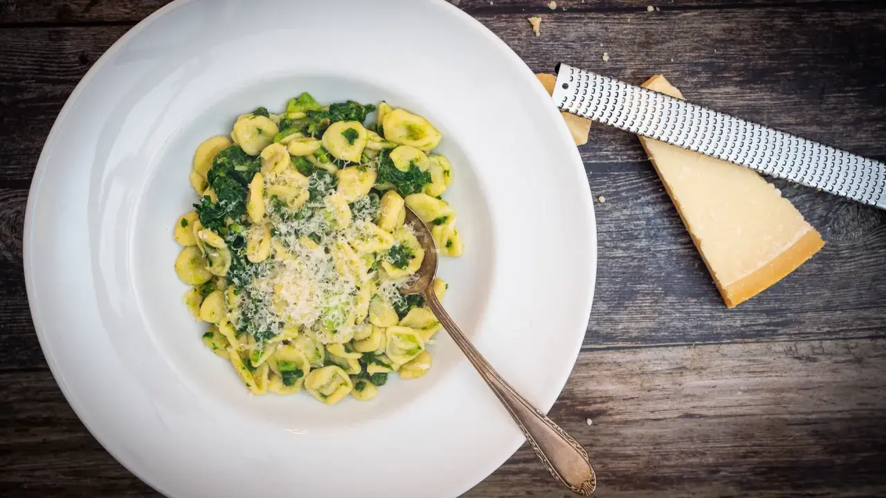 Orecchiette mit Cime di Rapa, frisch geriebenem Parmesan und einem Löffel auf einem Holztisch.