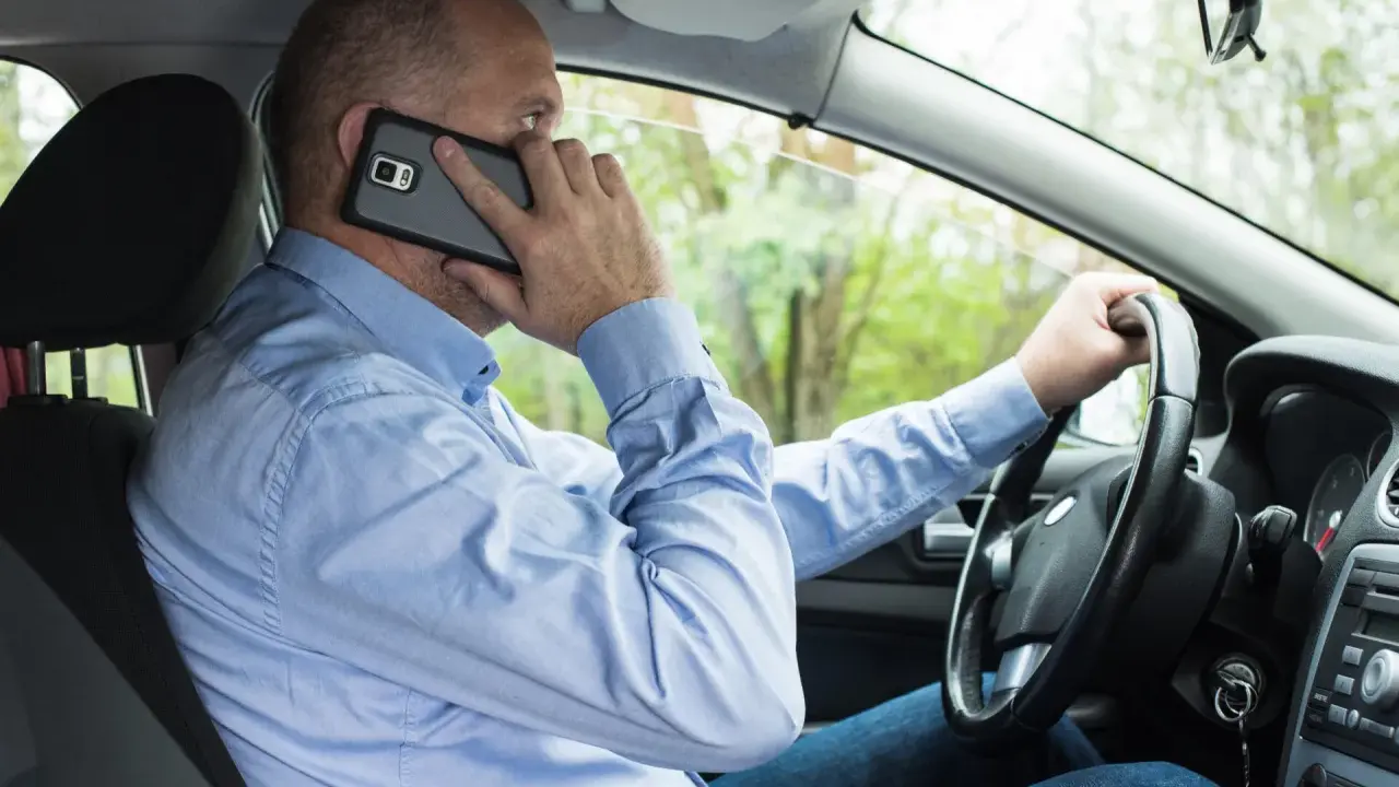 Mężczyzna za kierownicą rozmawia przez telefon, co może skończyć się mandatem.