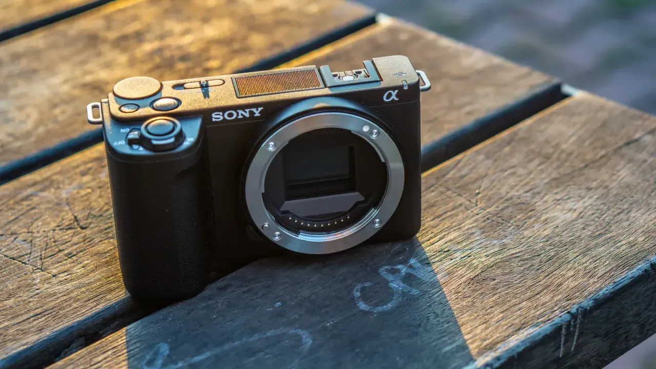 Czarny aparat Sony Alpha ZV-E10 bez obiektywu leży na drewnianym stole, oświetlony ciepłym światłem zachodzącego słońca.