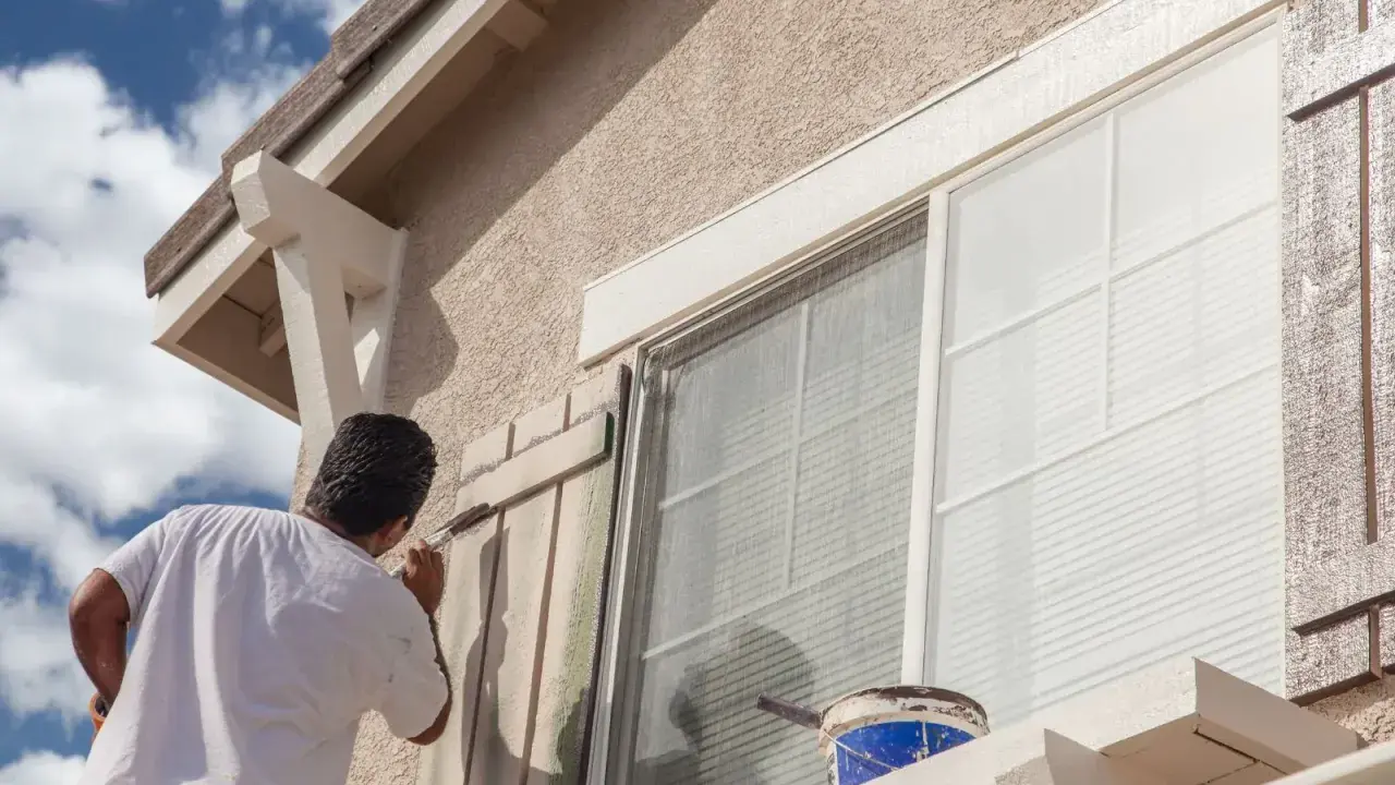 Un hombre pinta las contraventanas de una casa. El trabajo de pintar casas por fuera es esencial para su mantenimiento.