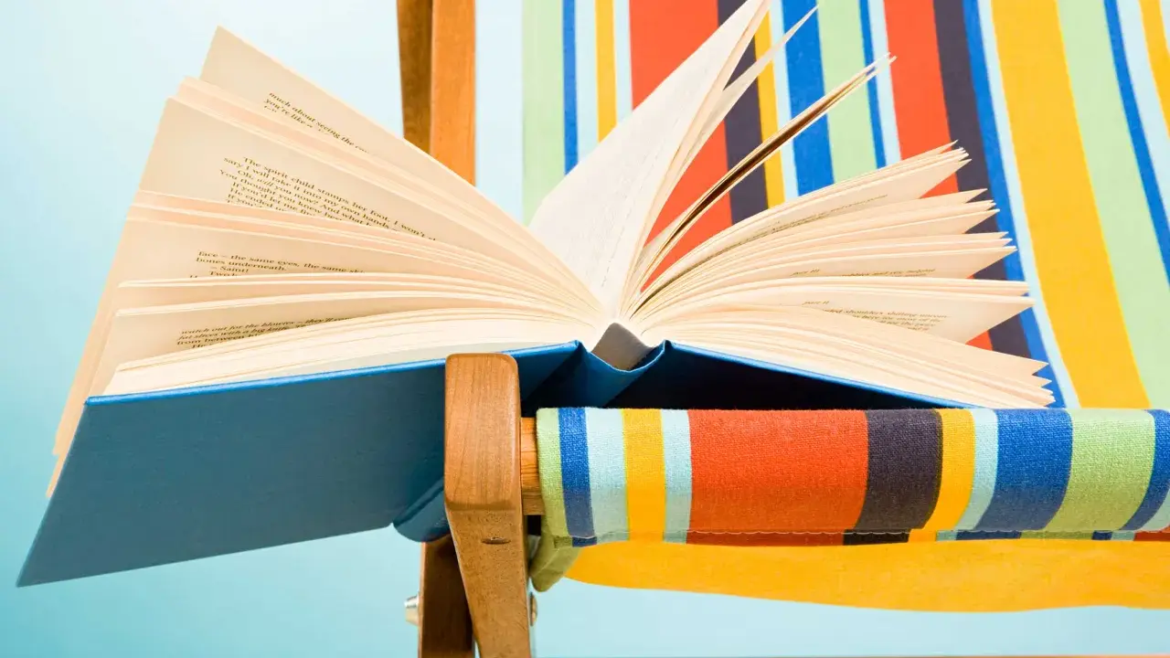 Un libro aperto, pieno di classici della letteratura, appoggiato su una sdraio a righe colorate.