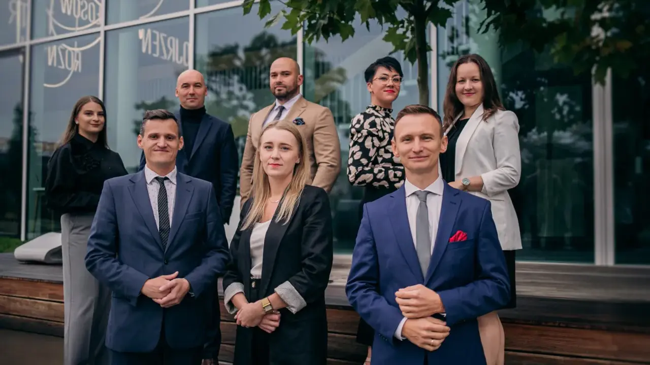 Grupa profesjonalistów w garniturach i eleganckich strojach pozuje przed nowoczesnym budynkiem.