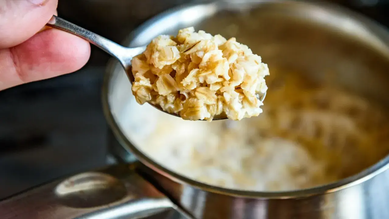 Łyżka gotowanych płatków owsianych, które pomagają obniżyć cholesterol. W tle garnek z owsianką.