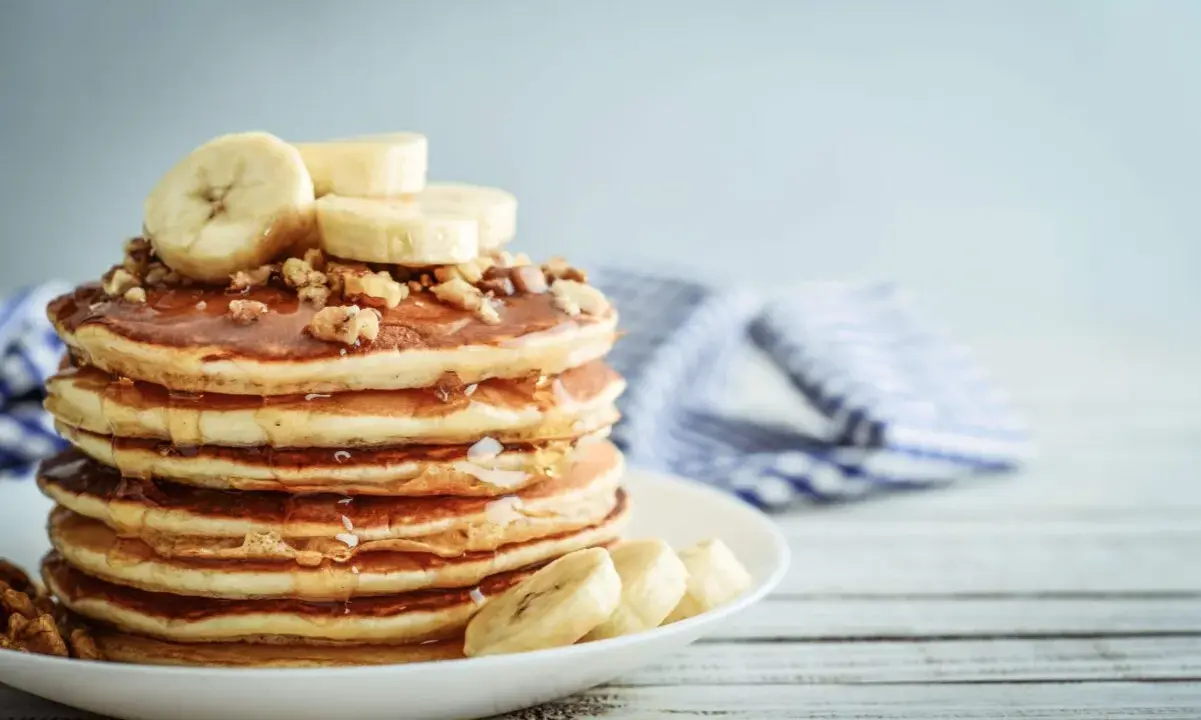 Una pila de tortitas de plátano cubiertas de miel y nueces, con rodajas de plátano fresco encima.