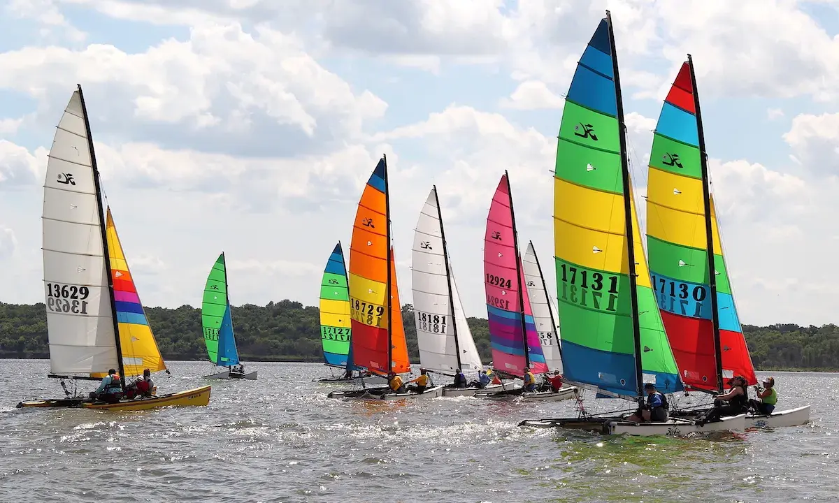 Course de Hobie Cat 18, voiles multicolores et blanches, sur l'eau par temps nuageux. Fiche technique du Hobie Cat 18.