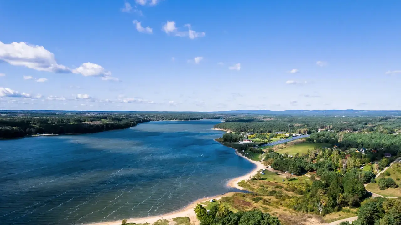 Malownicze jezioro Chańcza otoczone lasami, z piaszczystą plażą i zabudowaniami w tle.