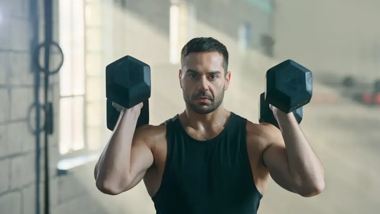 Mann hebt Hanteln im Fitnessstudio. Geduld ist der Schlüssel, wenn man fragt: Muskelaufbau wann sichtbar?