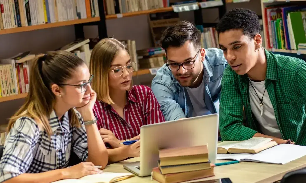 Studenci pochłonięci nauką historii przy laptopie w bibliotece.