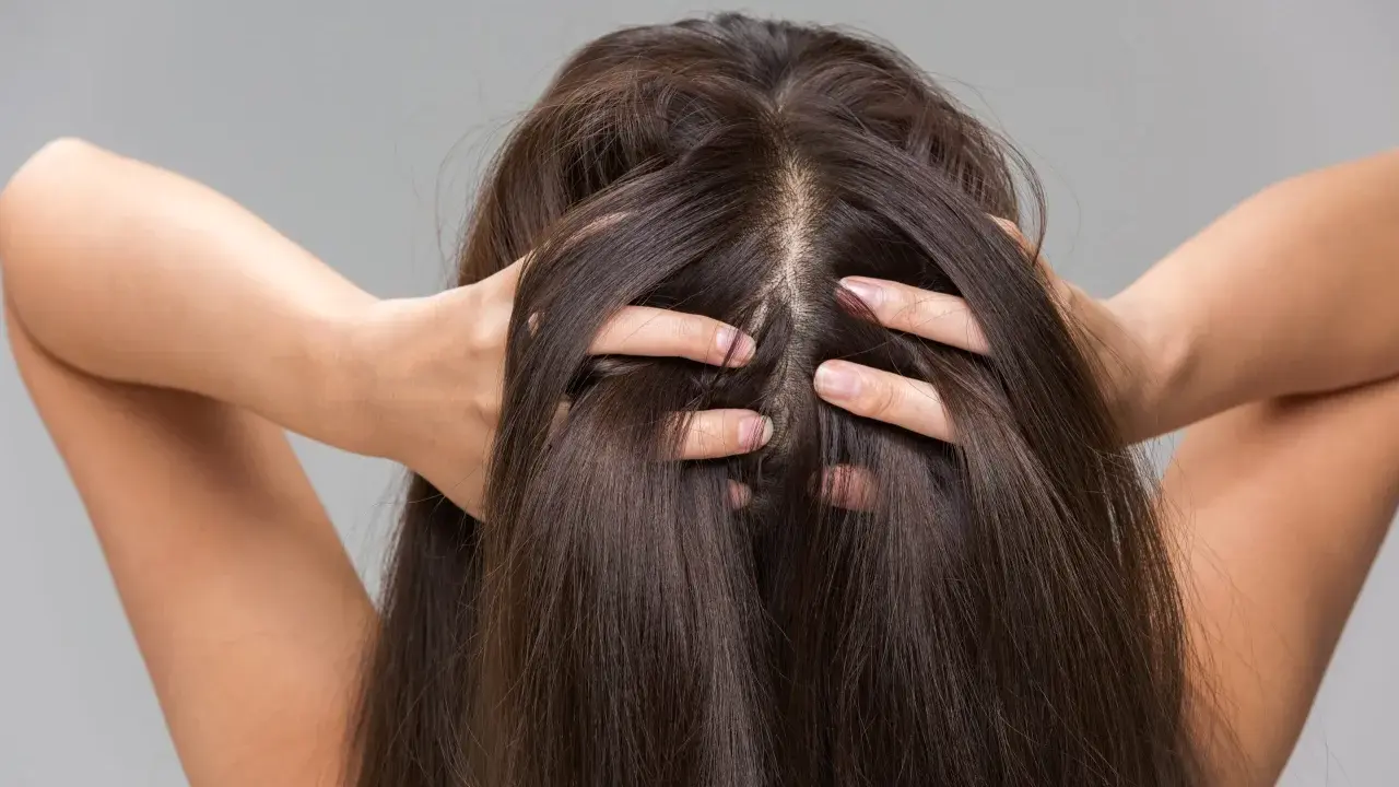 Une femme se touche les cheveux, montrant comment hydrater son cuir chevelu pour des cheveux sains et brillants.