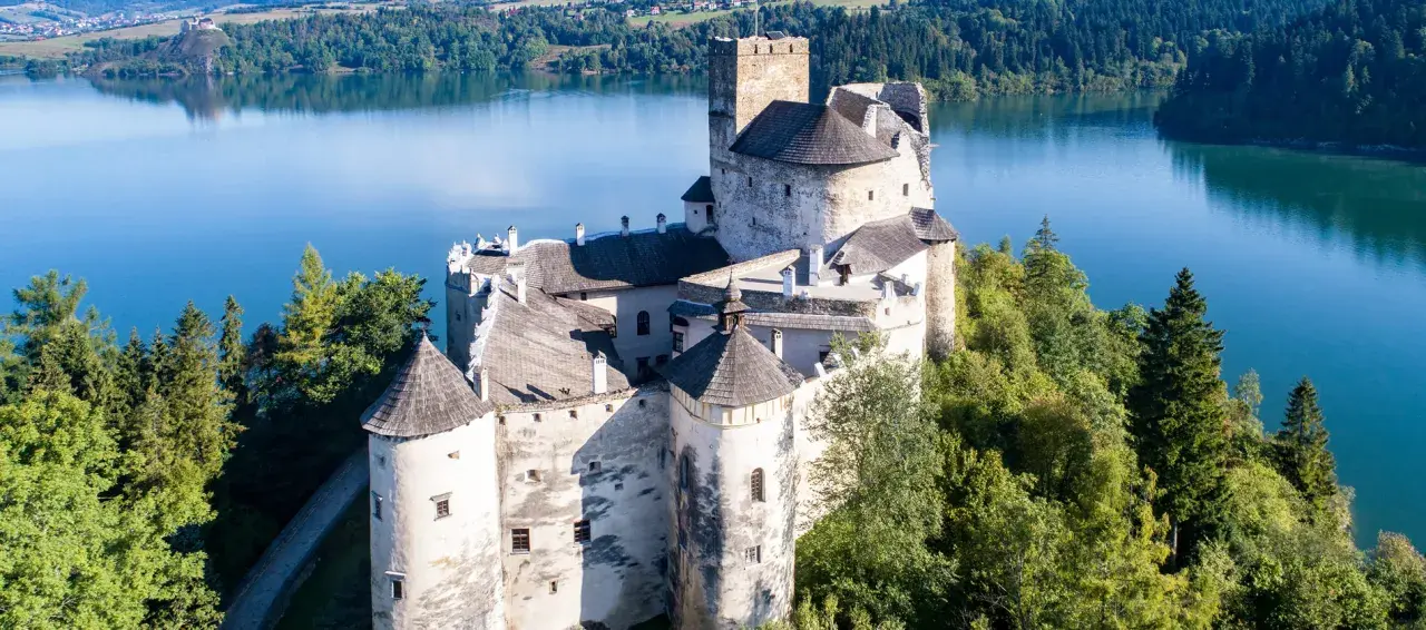 Zamek Dunajec, majestatyczna twierdza na skale, otoczona zielenią i błękitną wodą jeziora.