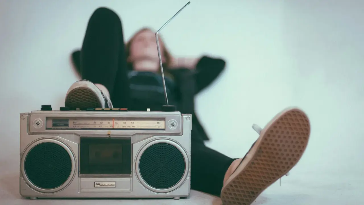 Osoba relaksuje się przy radiomagnetofonie, słuchając muzyki. To pokazuje, jak łatwo dotrzeć do odbiorców, co jest jedną z **zalet reklamy radiowej**.