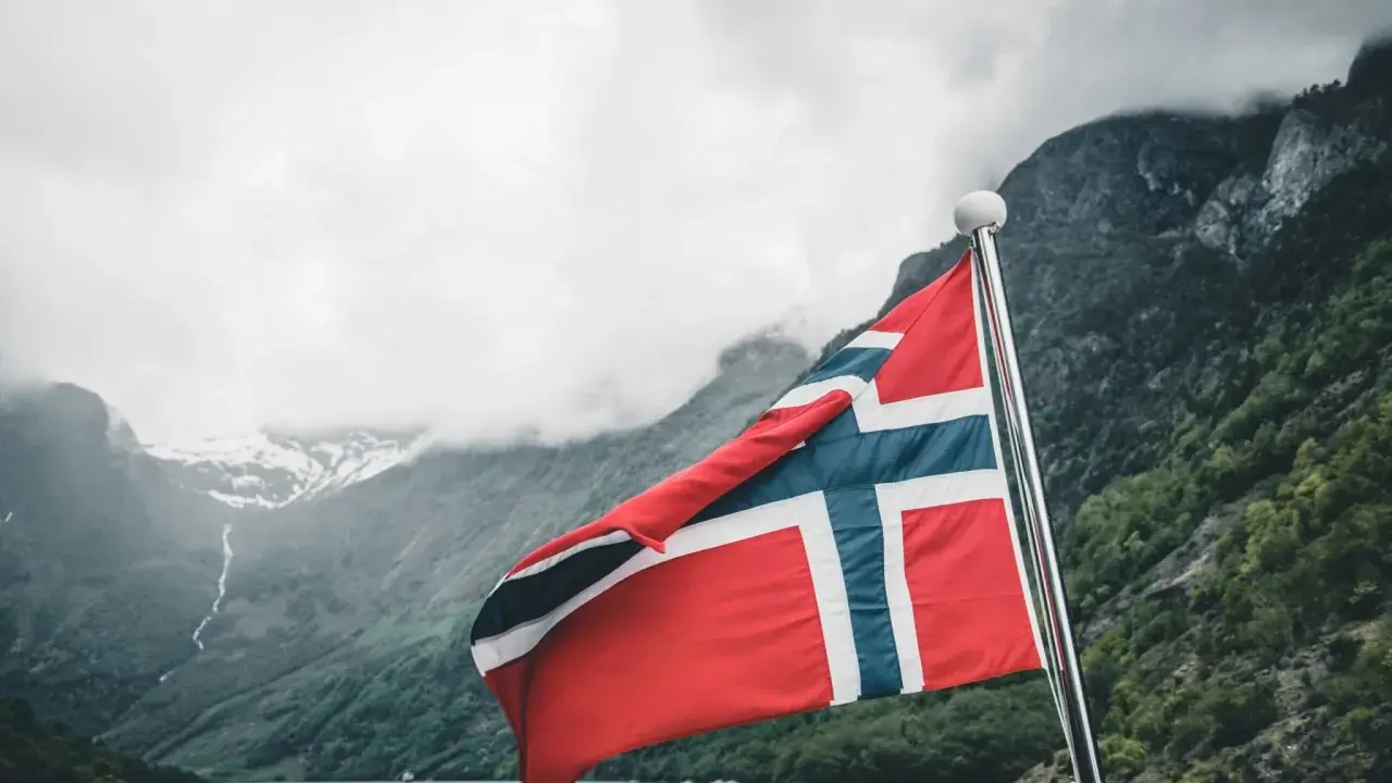 Norweska flaga na tle fiordu. Marzenia o wysokich zarobkach w Norwegii stają się rzeczywistością.