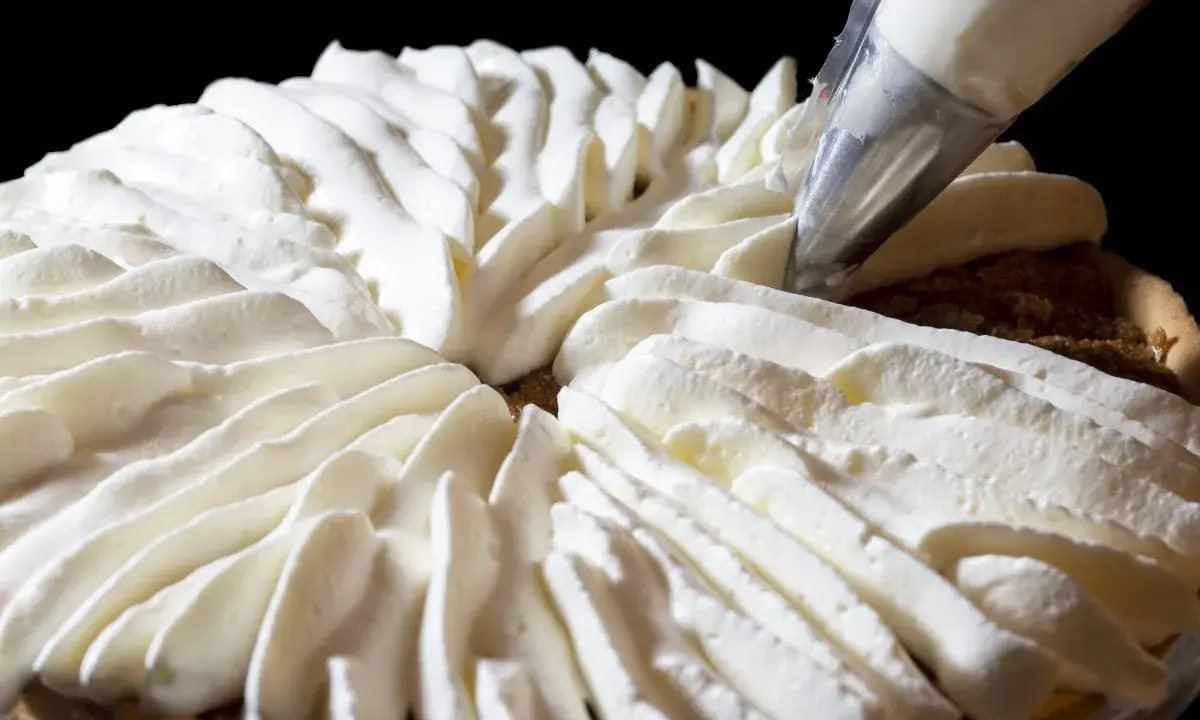 Garniture d'une tarte avec une poche à douille, évoquant la recette crémeux vanille Michalak.