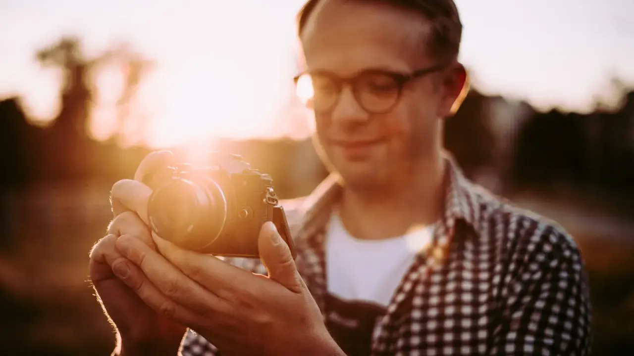 Mężczyzna w okularach trzyma aparat Olympus, łapiąc magiczne światło złotej godziny.