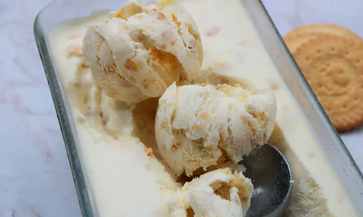 Pyszne lody ciasteczkowe w szklanym naczyniu, z widocznymi kawałkami ciastek i gałkami lodów. Obok leży okrągłe ciastko.
