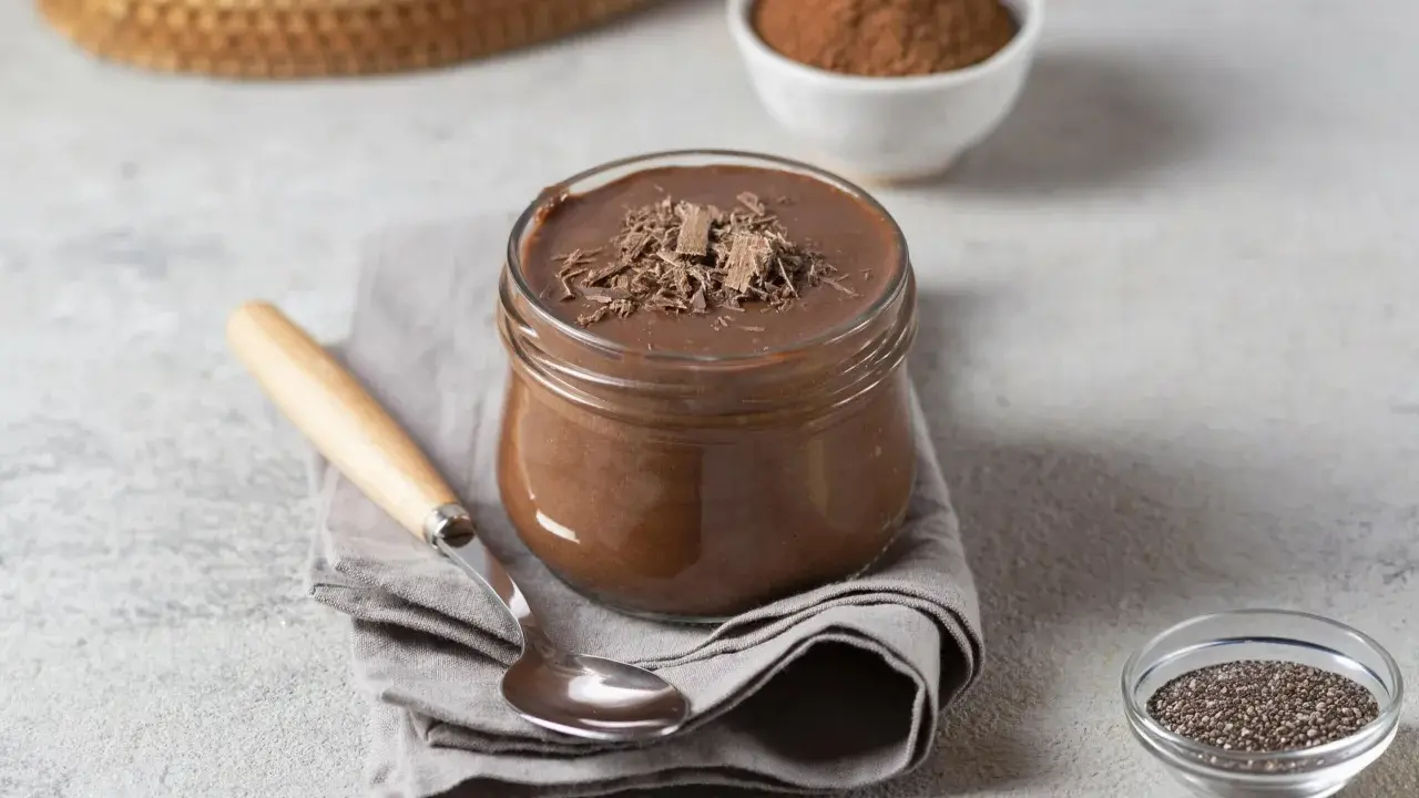Pudding proteinowy z czekoladą, idealny na deser. Obok nasiona chia i kakao, sugerujące, z czym jeść.