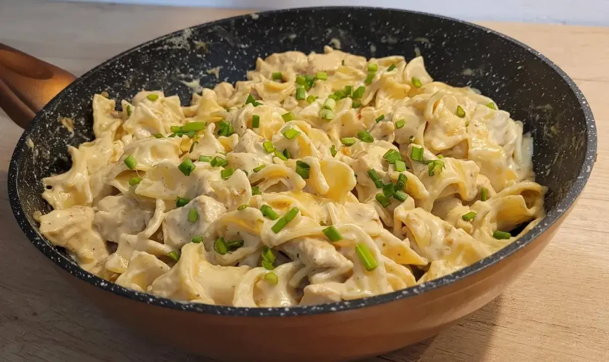 Tagliatelle z kurczakiem w sosie śmietanowym, posypane szczypiorkiem, podane w patelni. Pyszne danie gotowe do spożycia.