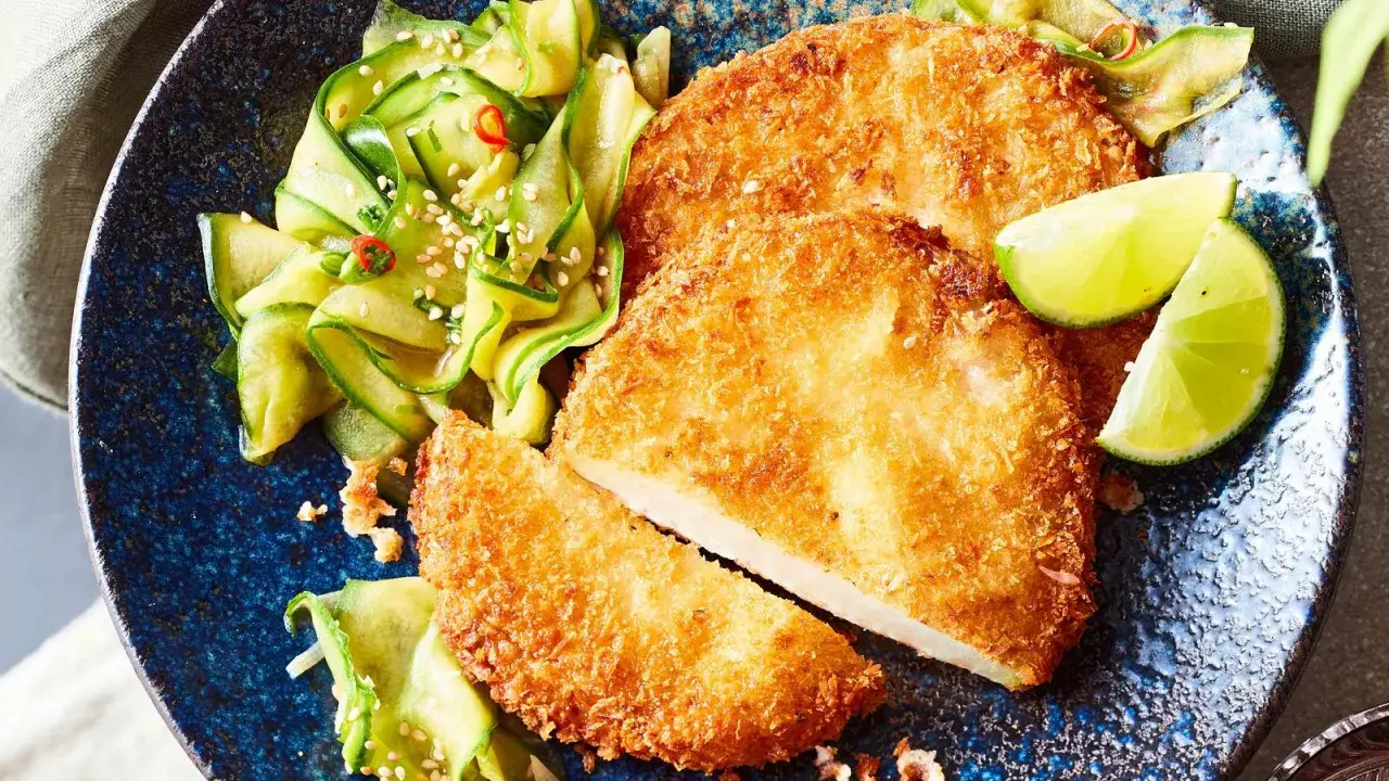 Knuspriges Kohlrabi-Schnitzel mit Gurkensalat und Limettenspalten auf blauem Teller.