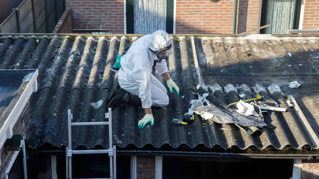 Travailleur en combinaison intégrale sur un toit en fibrociment, préparant le terrain pour une nouvelle peinture. Quelle peinture pour recouvrir peinture au plomb ?