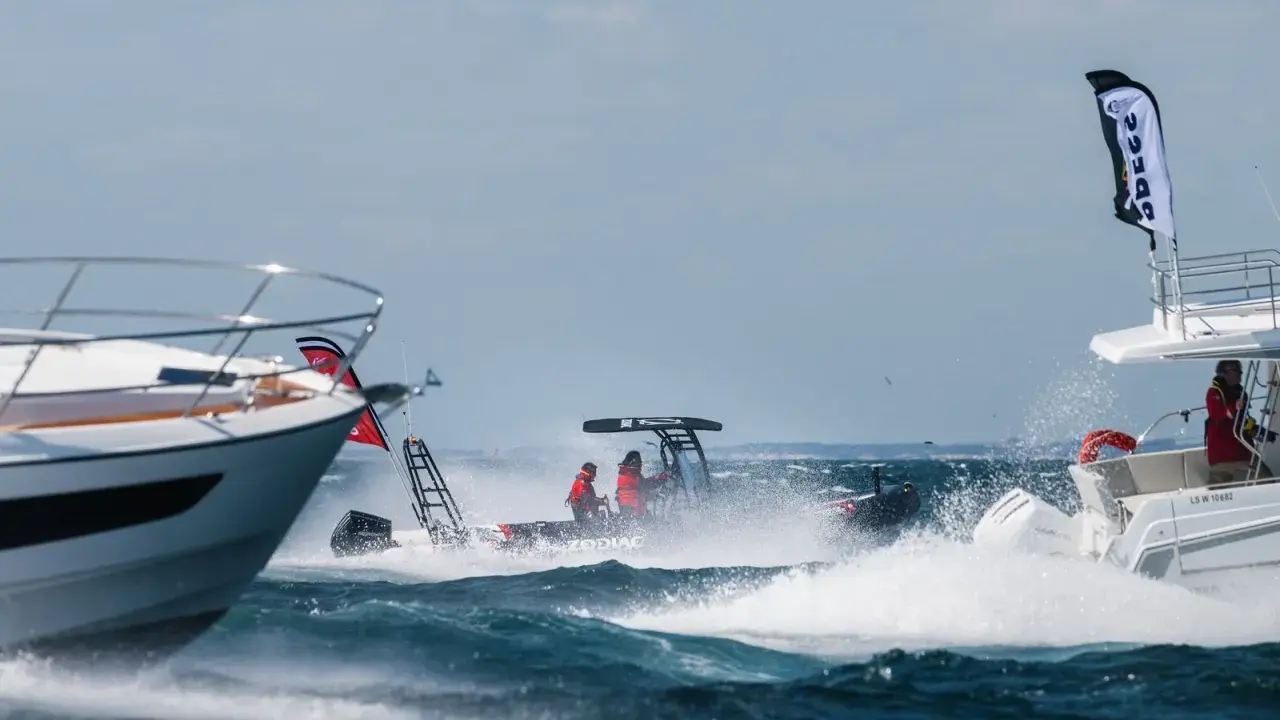 Trois bateaux en pleine navigation, éclaboussures d'eau, ciel bleu. L'un d'eux, un Zodiac, fend les vagues avec deux personnes à bord.