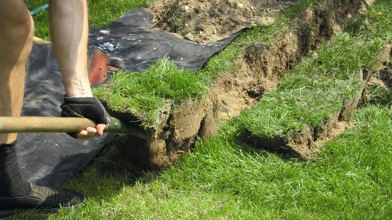 Osoba kopie rów, przygotowując teren pod układanie kabli w ziemi zgodnie z normą.