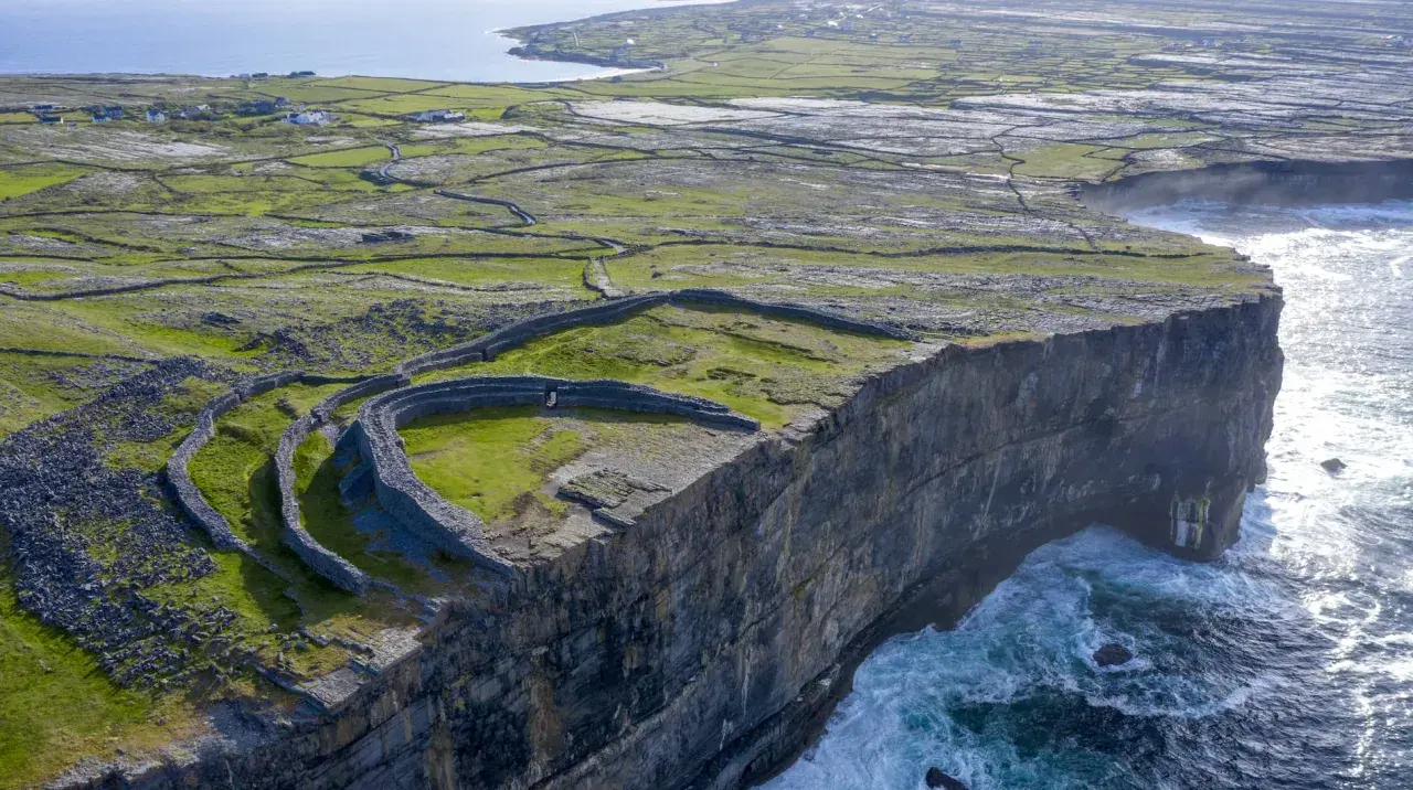 Steile Klippen und alte Steinmauern auf einer grünen Insel vor Galway, Irland. Wellen schlagen gegen die Felsen.