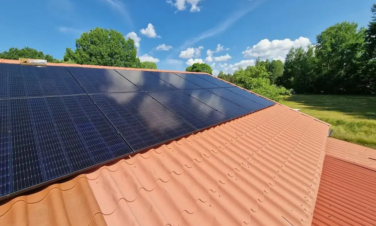 Solceller på ett tegeltak, redo för besiktning. Solen skiner på de mörka panelerna mot en blå himmel med vita moln.