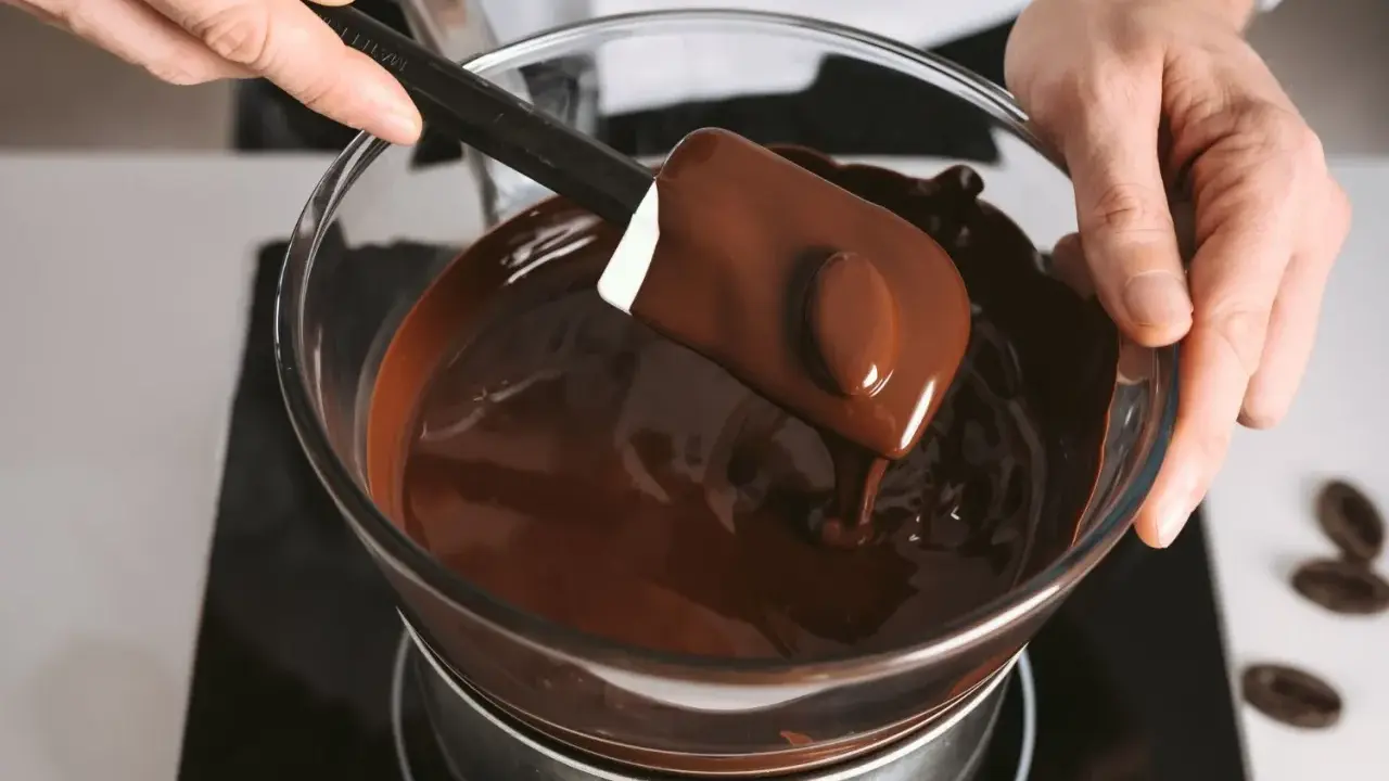 Un chocolat qui ne fond pas ? Ce n'est pas le cas ici ! Une spatule mélange du chocolat fondu brillant dans un bol en verre au-dessus d'un bain-marie.