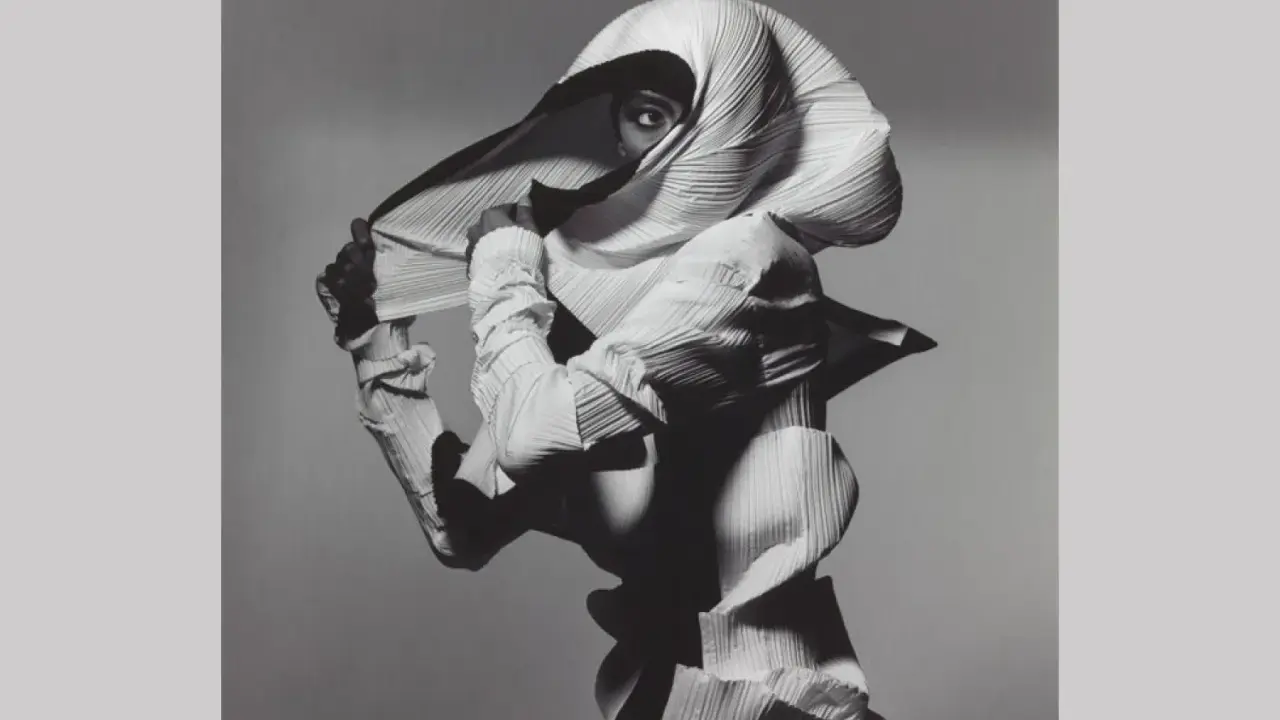 Modella con un abito plissettato bianco, un'opera d'arte di Irving Penn, che nasconde il viso tranne un occhio penetrante.
