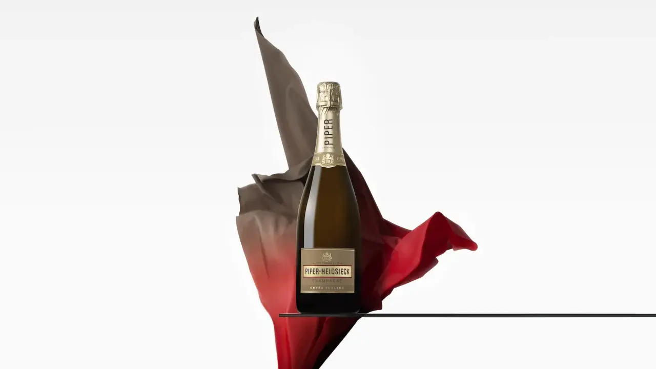 Eine Flasche Piper Heidsieck Cuvée Sublime, umhüllt von fließenden roten und braunen Stoffen, auf einer Glasplatte.