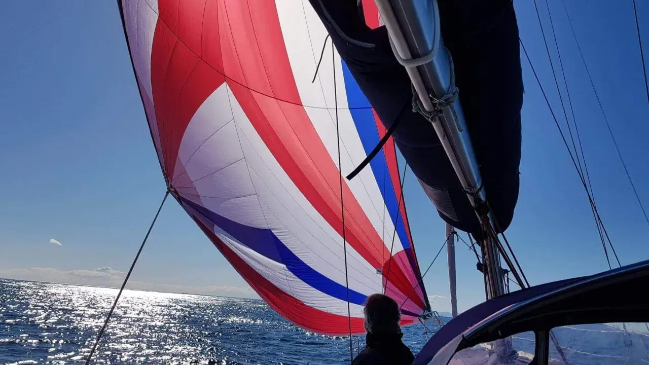 Voile colorée gonflée par le vent, un tableau longueur sandows sur fond de mer scintillante et ciel bleu.