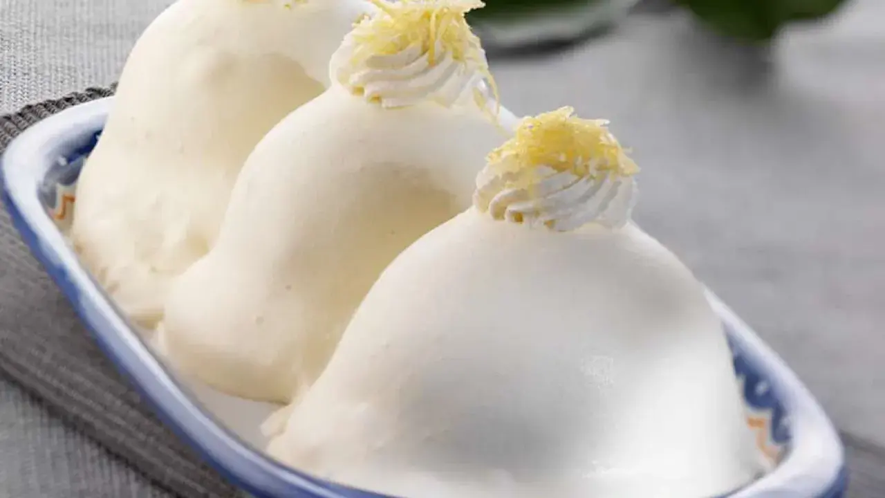 Tre deliziose delizie al limone, guarnite con panna e scorza di limone, in un piatto blu e bianco.