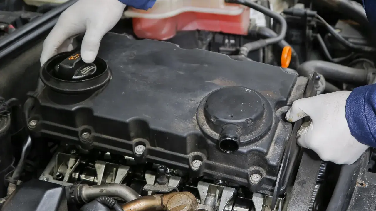 Mechanik w białych rękawiczkach sprawdza stan odmy silnika, demontując pokrywę zaworów.