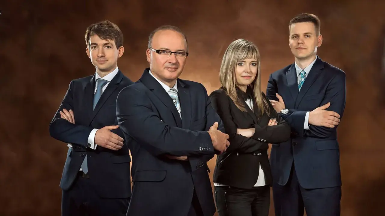 Cztery osoby w garniturach stojące z rękami skrzyżowanymi na piersiach.