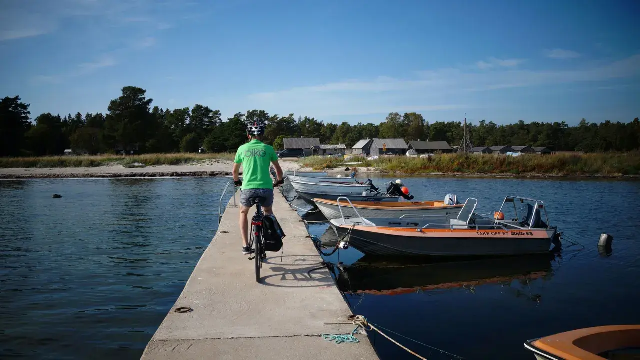 En cyklist på en brygga med båtar vid en svensk kust. Perfekt för att utforska cykelleder Sverige.
